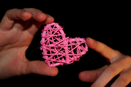 A child's hand holds a pink rattan heart on a black backgroundの写真素材
