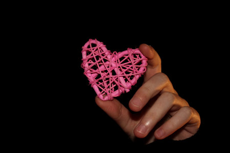 A child's hand holds a pink rattan heart on a black backgroundの写真素材