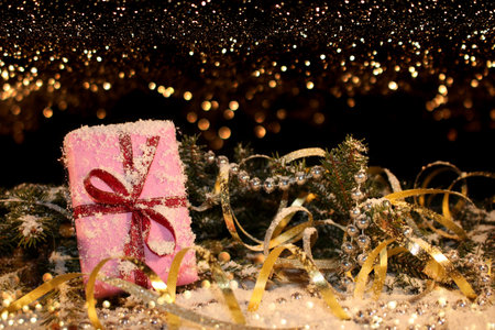 Christmas background with a pink gift on the background of a snow-covered green fir tree on a shiny background.の写真素材