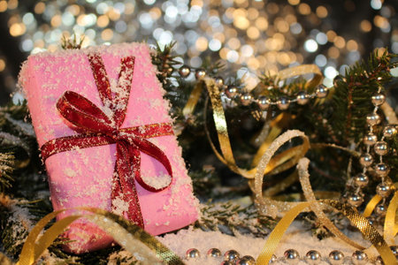 Christmas background with a pink gift on the background of a snow-covered green fir tree on a shiny background.の写真素材
