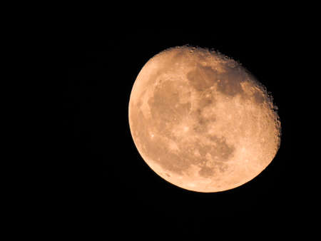 Detailed closeup of big and pink waning gibbous phase moon in black background, showing craters