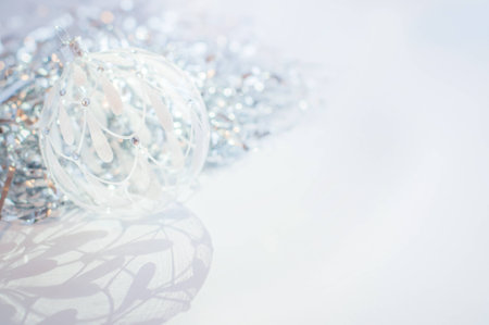 White glass decoration ball on a white background with silver tinsel behind with a beautiful shadow. New Year and Christmas decoration.の写真素材