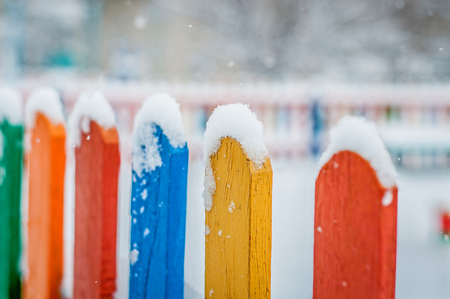 Colorful wooden fence under snow. Blue, red, yellow, orange fence parts under snow.の写真素材