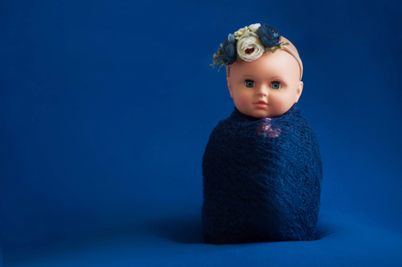 Baby doll toy photodraphed in a newborn style. Wrapped in dark blue woolen fabric on a blue background. Vertical posture.の写真素材
