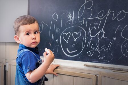 Little boy standing near school blackboard with a piece of chalk
