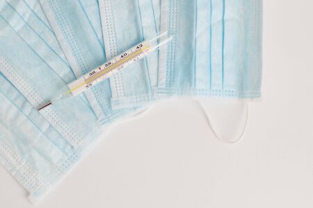 Pile of blue medical masks and analogue medical thermometer. Medical respiratory bandage face on white background. Prevention and diagnostics of the spread of virus and epidemic.の写真素材