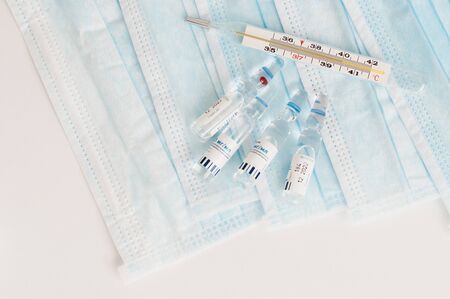 Sterile medical blue masks, vials with vaccine and analogue thermometer on white background. Flu season concept. Epidemics prevention concept.の写真素材
