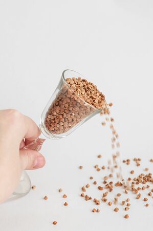A hand scattering small glass of buckwheat - traditional Russian meal - on white background....