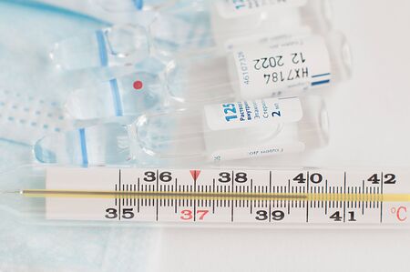 Sterile medical blue masks, vials with vaccine and analogue thermometer on white background. Flu season concept. Epidemics prevention concept.の写真素材