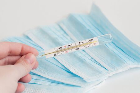 A hand holding analogue medical thermometer showing high temperature.