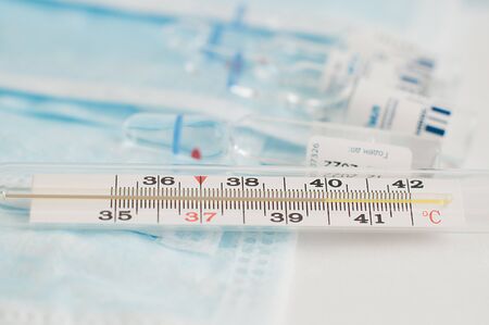 Sterile medical blue masks, vials with vaccine and analogue thermometer on white background. Flu...