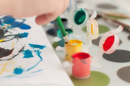 Kid's hand is painting colorful picture with gouache. Remote education concept during quarantine.の写真素材