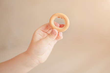 babies hand holding a bagel on a solid color backgroundの写真素材