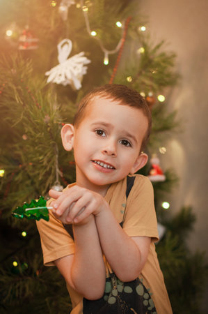 Little boy having fun near a christmas tree with a candy in shape of a fir tree at homeの写真素材