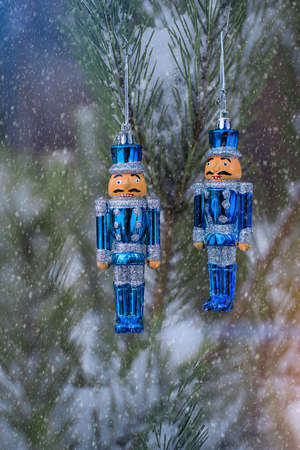 A pair of tin solders hanging on a snowy fir tree in the forest outdors. Christmas toys.