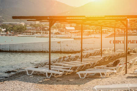 white sunbed standing on a rocky seashore on summer morningの写真素材