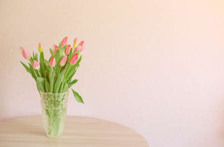 A bouquet of colorful young spring tulips wrapped in a glass vase on a tableの写真素材
