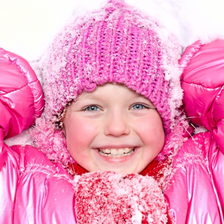 Little happy girl in winter pink hat in snow の写真素材