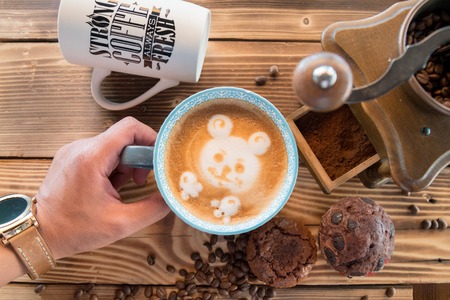 Man hands holding a cup of coffee with foam next to the coffee grinder on wooden table, top viewの写真素材