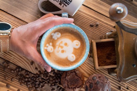 Man hands holding a cup of coffee with foam next to the coffee grinder on wooden table, top viewの写真素材