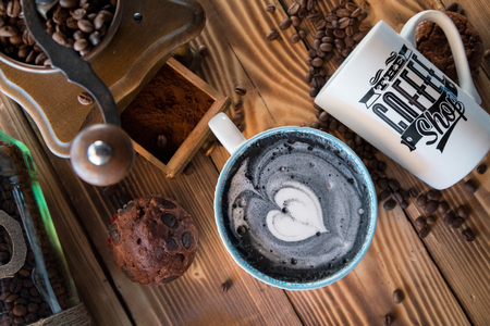 Black latte with black heart foam in art ceramic cup at old wooden board, top viewの写真素材