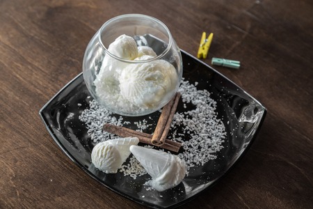 White Ice cream cone with coconut chips on a black plate on dark wooden tableの写真素材