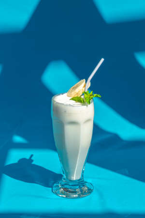 Banana milk smoothie with mint and drinking straw on abstract blue background.の写真素材