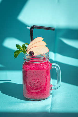 Pink smoothie with wild blueberry in mason jar with mint and straw on abstract blue background.の写真素材