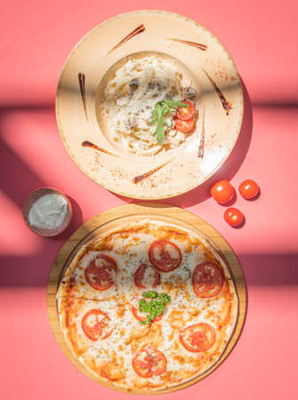 Italian fettuccine pasta and traditional pizza margherita with tomato on pink abstract background.の写真素材