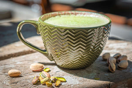 Pistachio coffee with tasty milk foam and pistachio nuts on old wooden table.の写真素材