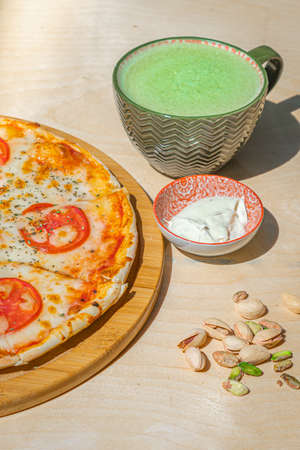 Japanese iced Matcha latte tea with pizza margherita and pistachios on wooden table.の写真素材