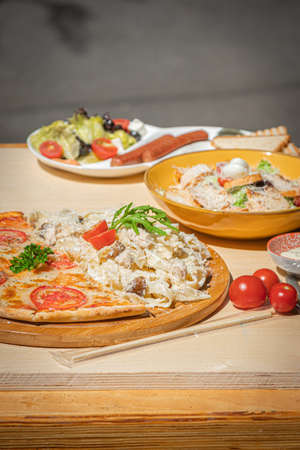 Breakfast wooden table with pizza, pasta, sausages and salad.