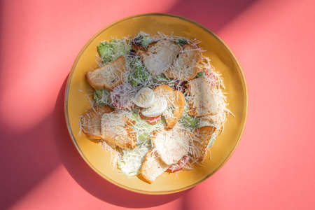 Cesar salad with roasted chicken meat on yellow plate on colorful pink background.