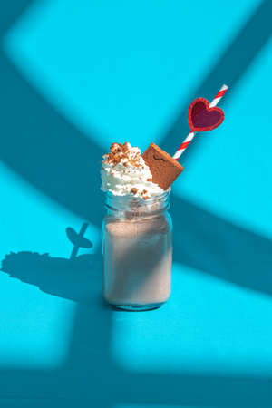 Milkshake chocolate in jar with a straw and heart on blue background with abstract shadows.の写真素材