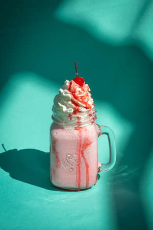 Milkshake with a cherry and whipped cream on mint turquoise background with abstract shadows.の写真素材