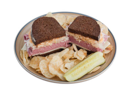 Reuben sandwich on a plate with pickle and potato chipsの写真素材