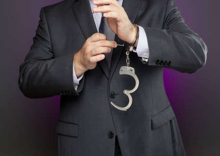 Businessman is using a key to unlock a pair of handcuffs. Image can be used metaphorically to represent business concepts about removing restrictions.の写真素材