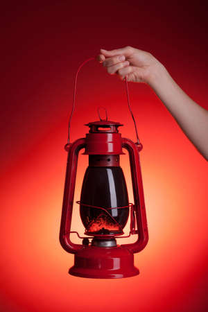 A woman holds up a sooty kerosene lantern. Red backdrop with orange spotlight gives the impression of light emanating from the lantern. の写真素材