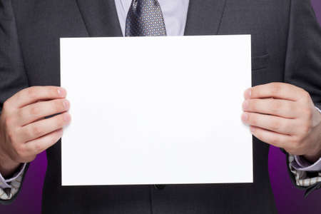 A man in a business suit holds a blank paper sign. Photographed with studio lighting. Color filter...