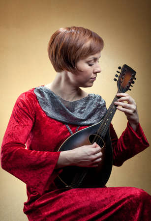 A woman wearing a red velvet tunic strums a mandolin.の写真素材