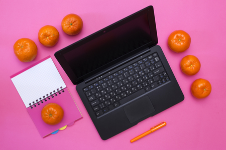 Laptop, notebook, pen and tangerines on a pink backgroundの写真素材
