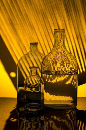 Still life with glass bottles on a yellow background with shadowsの写真素材