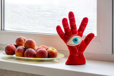 Protective amulet in the shape of an open palm and eye made of felted wool on a peach windowsillの写真素材