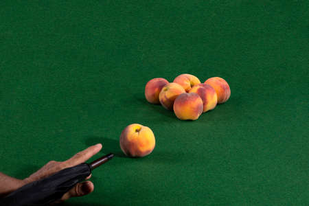 Hand with an umbrella and ripe peaches on a billiard table
