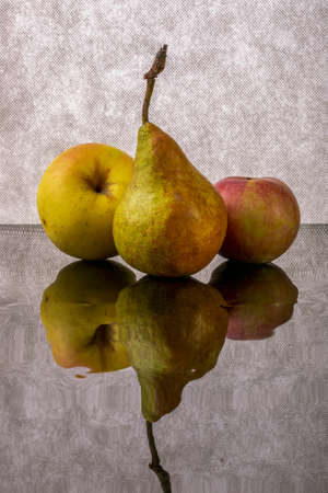 Ripe apples and pear on reflective surface on gray backgroundの写真素材