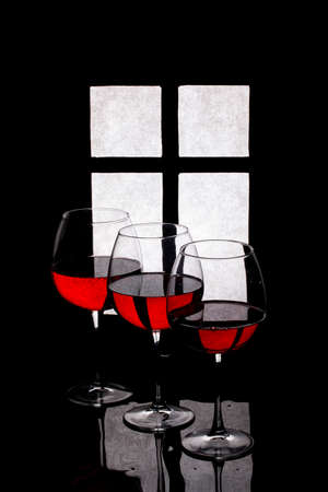 Still life with glasses and red wine against the background of a window silhouetteの写真素材