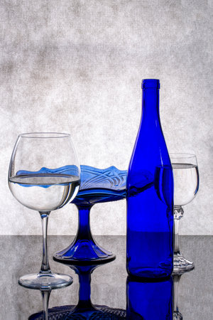 Still life with blue bottle, glass and blue vase on gray backgroundの写真素材