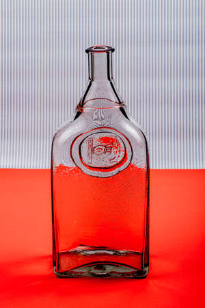 Glass transparent bottle on red table on striped backgroundの写真素材