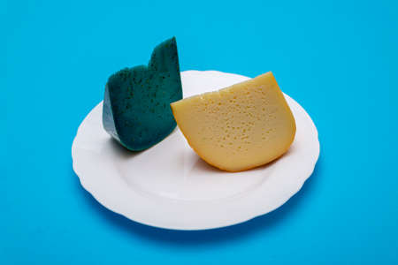 Pieces of cheese on a white plate on a blue backgroundの写真素材