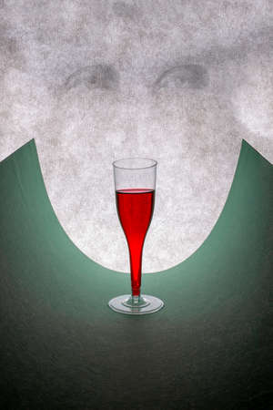 Glass with red wine on a curved green leaf and human eyes on a gray backgroundの写真素材